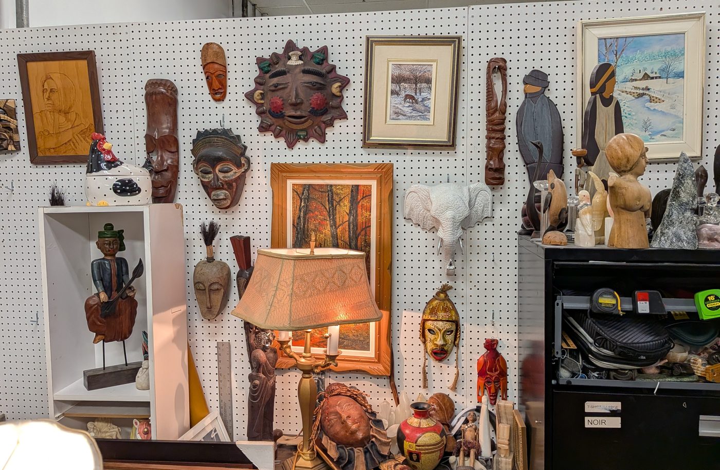 Mur du kiosque couvert de masques sculptés, d'un masque soleil, de tableaux et de statuettes en bois